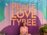 A woman seated below a wall mural that says, Peace Love Tybee. ." T