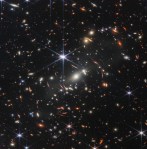 hundreds of pinpoints of light, each a galaxy. They are dots and streaks of many colors - yellow, blue, red. There is a starburst one in the center.