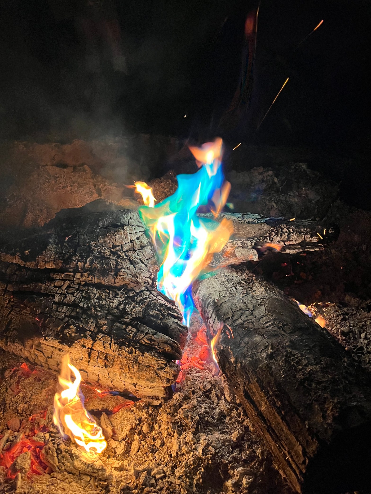 A blue, green, and yellow flame with burned branches around it