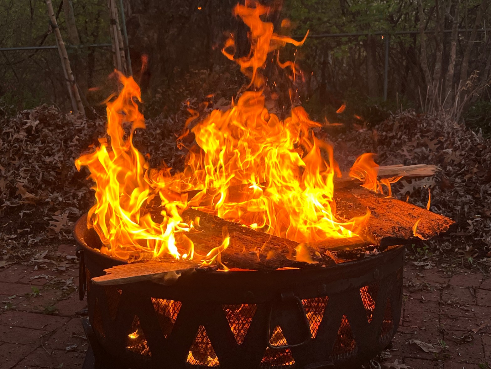 a blazing circular fire pit filled with wood. There is a brick patio in the background