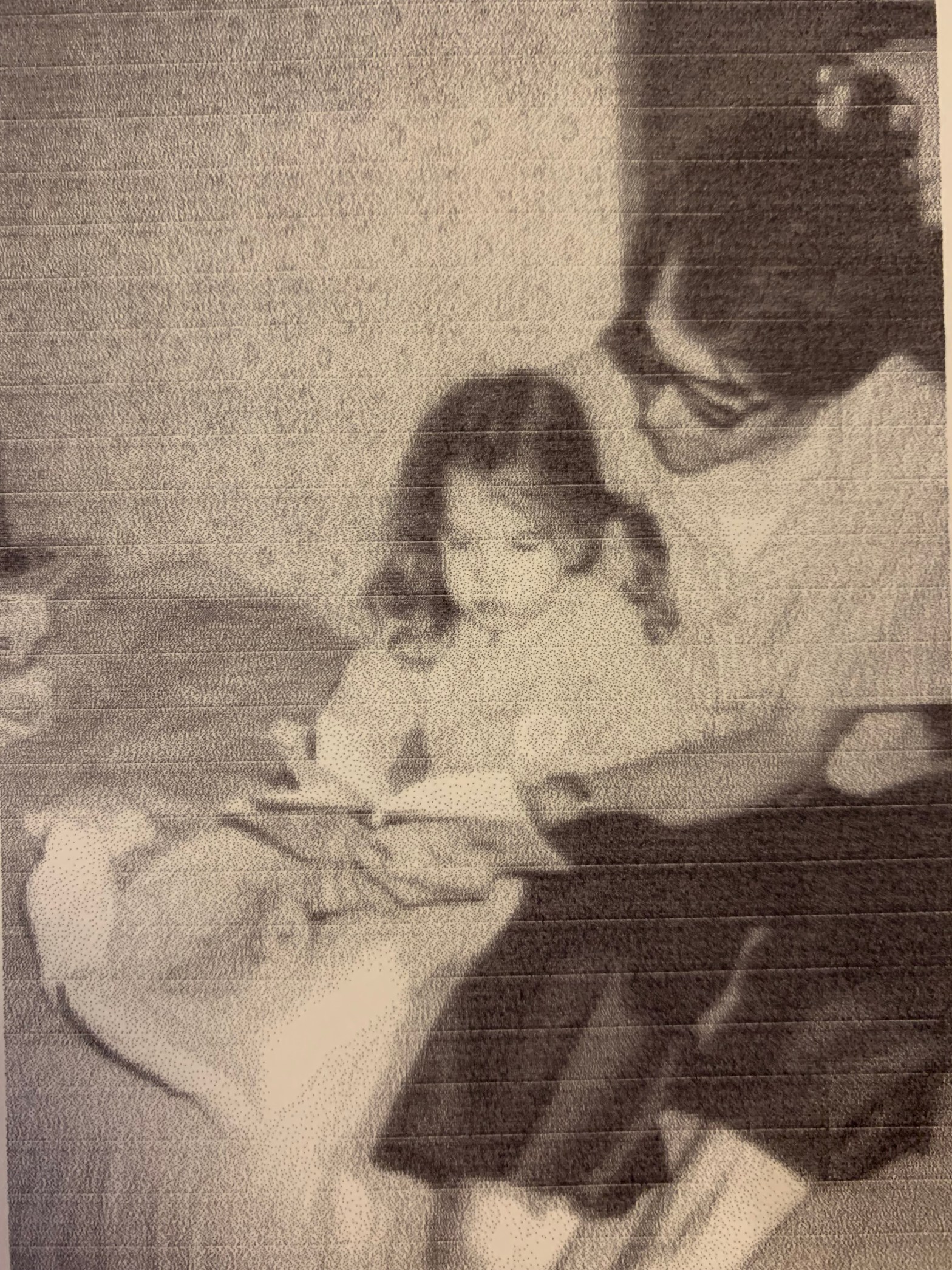 In the middle of the picture, a small girl with pigtails is seated on a bed looking at a book held by a man to the right. He has dark hair and dark-rimmed glasses.