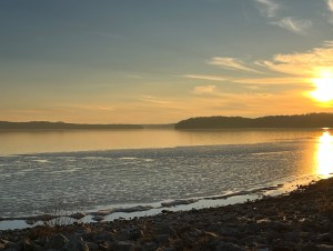 A picture of a lake from the beach. There is a sunset to the right