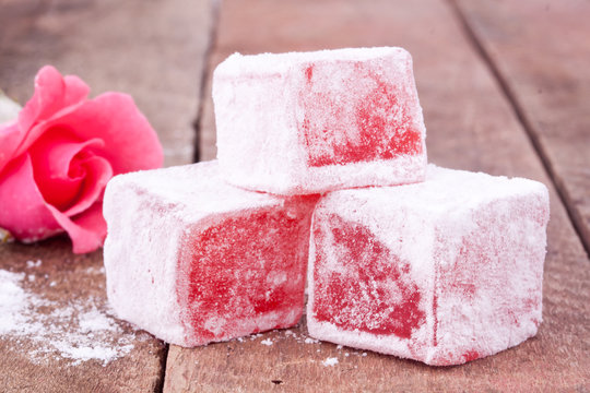 A picture of Turkish Delight, blocks of squishy pink candy with a powdery coating. There's a pink rose in the background.